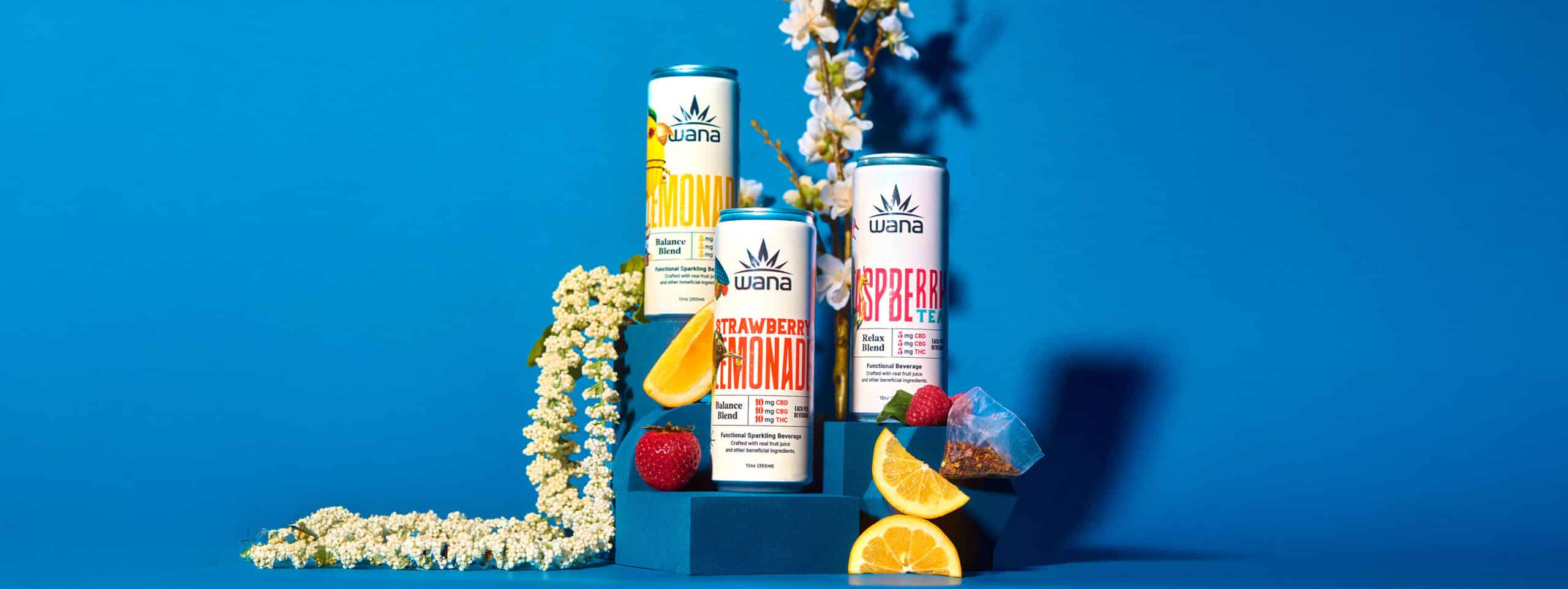 A tiered pedestal displaying three cans of Wana's hemp-infused beverages: Lemonade, Strawberry Lemonade, and Raspberry Tea.